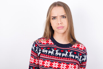 Displeased Young caucasian girl wearing christmas sweaters on white background frowns face feels unhappy has some problems. Negative emotions and feelings concept