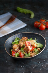 A bowl of delicious salad with fresh vegetables and chicken on a dark background. Healthy food.