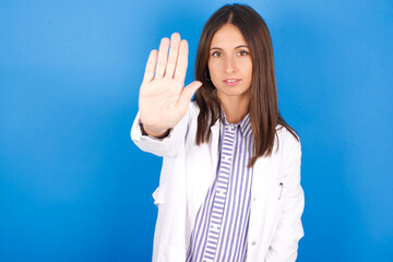 Young european doctor woman on blue background doing stop sing with palm of the hand. Warning...