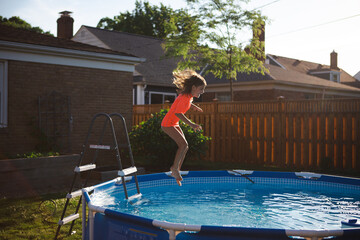 Girl leaping into backyard pool 