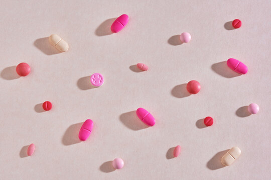 Randomly scattered colorful pills on a pink background