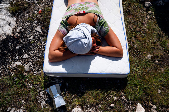 Girl sleeping outside on a mattress next to coffee maker