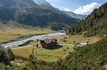 Fototapeta na wymiar Panoramic view on the Alpenrose mountain hut. Sun-flooded valley with turquoise mountain river . Berlin high trail in Zillertal Alps Nature Park.