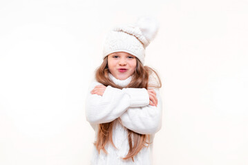 A little girl is freezing in a white knitted sweater and hat on an isolated background.