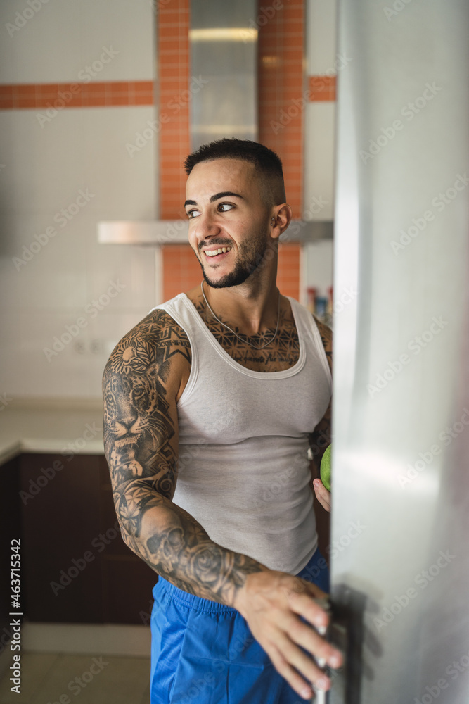 Canvas Prints Vertical shot of a tattooed Caucasian male athlete opening the fridge