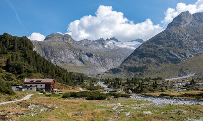 Fototapeta na wymiar Panoramic view on the Alpenrose mountain hut. Sun-flooded valley with turquoise mountain river . Berlin high trail in Zillertal Alps Nature Park.