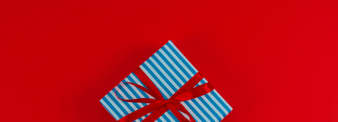 One blue striped gift box with ribbon lies in the middle on a red background