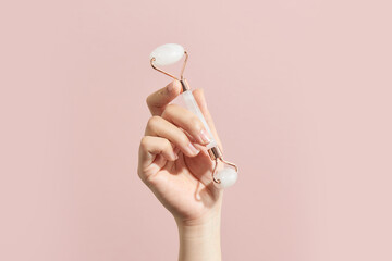 Female hands holding rose quartz facial massage roller