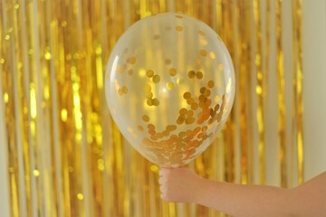 Childrens holidays concept.Birthday background. Balloon with gold kanfeti in a child's hand on a...