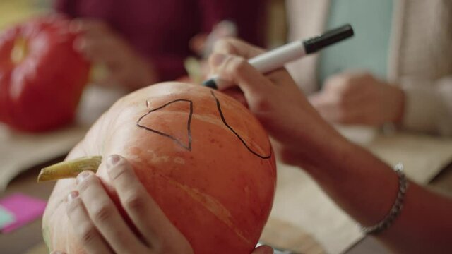 A man uses a marker to draw a mouth on a pumpkin