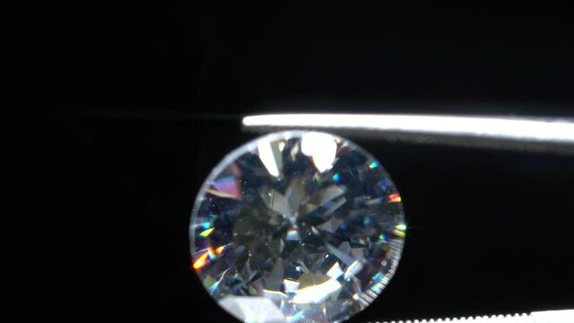 Loose diamond in tweezers selective focus. Macro shot of precious stone inspection for defects. Certification of brilliant cut diamond. Gemstone in clamp for making luxury jewelry. Natural material.