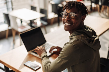 African man with laptop at the table. smiles and looks into the lens. distance communication,...