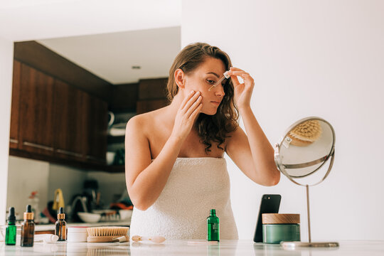 Woman using serum while looking in the mirror