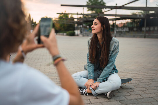 Young man taking picture of girlfriend on skateboard