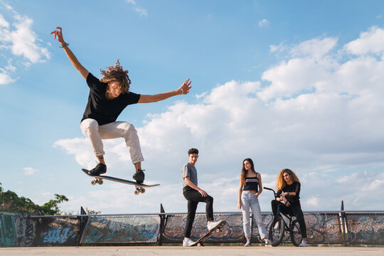 Young man doing skateboard stunts near friends