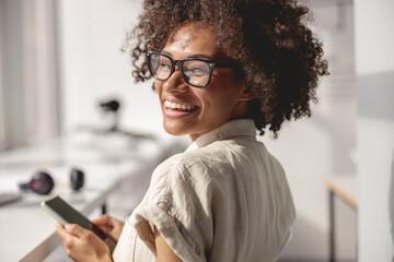 Close up of Afro American worker wearing glasses and using smartphone in the office