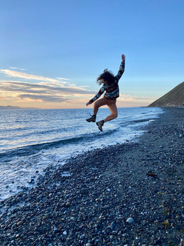 Teenage girl jumping high above waves and beach