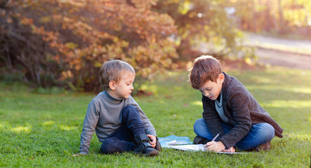 Naklejka na ściany i meble The kid is watching as the older brother next to him doing his homework sitting on the grass