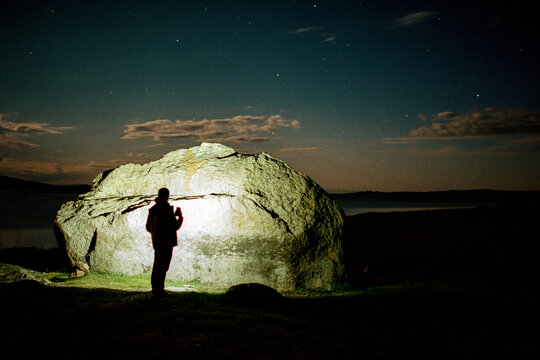Anonymous guy stands in front of a stone at night