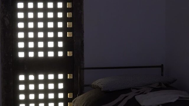 Barred window and bed with pillow in prison cell.