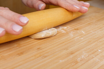 Piece of dough under a wooden rolling pin. Roll out the dough by hand.