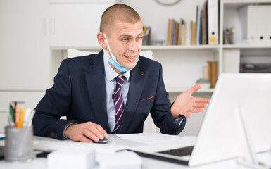 European businessman in mask having video conference on laptop in corporate modern office