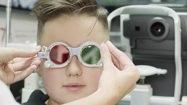 A female optometrist inserts a red and green lens into the phoropter. Eyesight examination in an ophthalmology clinic for a teenage boy
