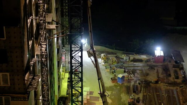 Construction workers pouring wet concrete using concrete spider hose or pump work at high-rise site in night