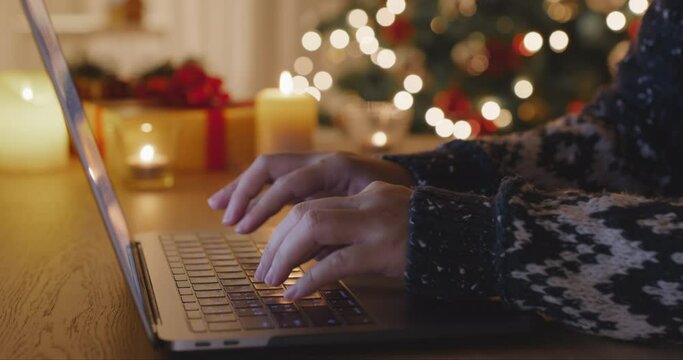 Close-up hand enter search gift card on web page sending Merry Xmas eve wishing text or chat on e-mail working on laptop at home. Good warm time cozy Night winter season with tree light inside house.