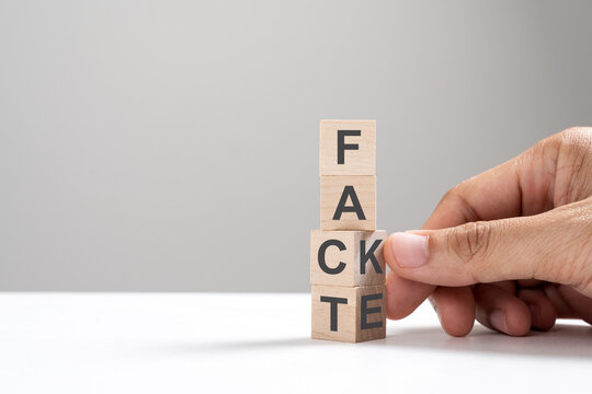 Hand flip wooden cube change the word from fake to fact