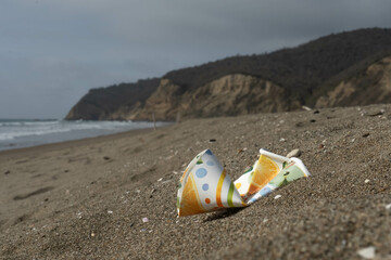 Plastic cup  polluting the beach next to mountains and the coastline