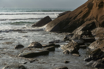 waves crashing into rocks on the beach during a sunny day