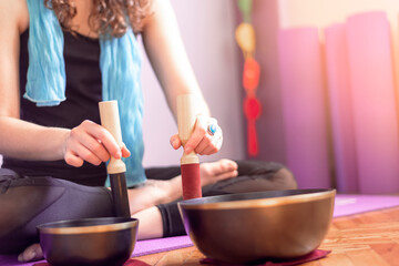 Obraz na płótnie Canvas Low section of a young caucasian woman playing tibetan singing bowls over a purple yoga mat on wooden floor. Concept of meditation and relaxation at home. Yogini. Selective focus