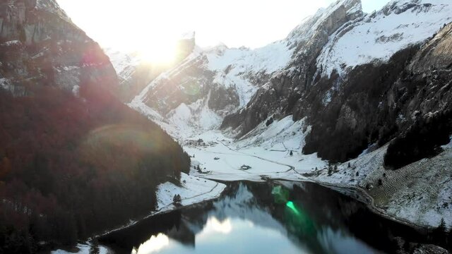 Aerial flyover alongside Seealpsee in Appenzell, Switzerland as the sunshine disappears behind the snow covered Alpstein peaks across the lake - 4k