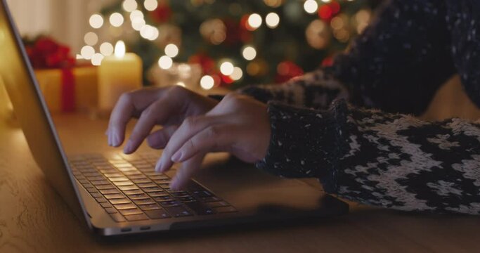 Close-up hand enter search gift card on web page sending Merry Xmas eve wishing text or chat on e-mail working on laptop at home. Good warm time cozy Night winter season with tree light inside house.