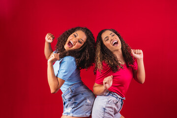 Portrait of happy young afro women friends dancing on red background.