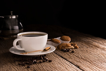 Coffee cup with cookie bread bakery or breakfast cake laying on a wooden table on a black needle background