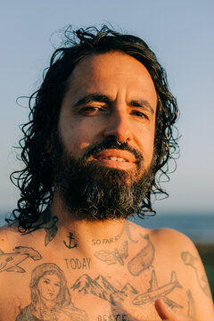 Bearded man with tattoo on his chest looking at camera