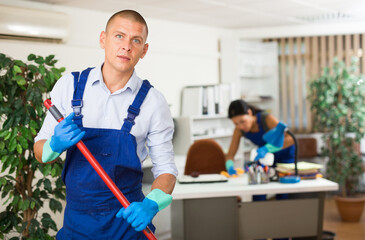 Obraz premium Positive male worker from cleaning service, wiping office floor with mop