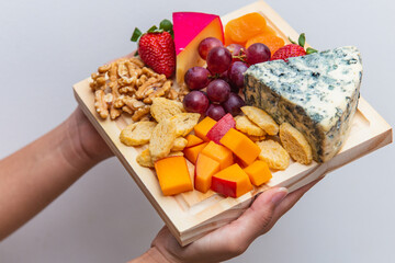 hands holding board with various cheeses