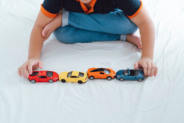 boy in a blue shirt lying and playing toy cars on the bed