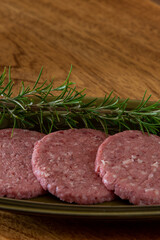 Raw burgers served on a green plate with rosemary branch