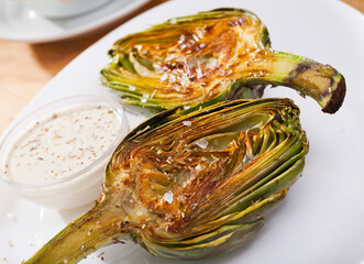 Delicious roasted halves of artichoke served with sea salt and sauce. Healthy vegetarian food..