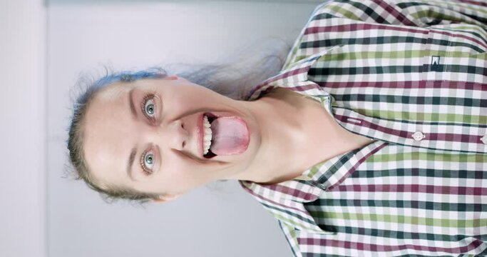 woman face close up. girl doing facial muscles workout. Make funny or scary grimaces; the tongue sticks out strongly and pulls to the chin, the eyes bulge, the eyebrows are raised. Lion face