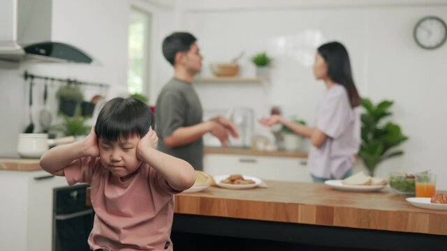 Asian boy kid use hands close ears because parents having fighting at home. Family problems cause children to have psychological problems in the future. Domestic problem in family.
