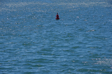 A single large red buoy marke No. 8 floating in the blue ocean water near a harbor entrance