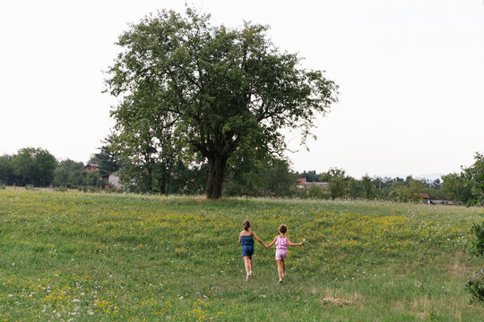 Two cheerful girls running over big green field