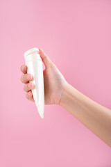 Woman's hands with a tube and a swatch of cream on a pink background. Cosmetic products concept.