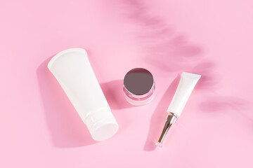 Set of skin creams on a pink background with shadows of leaves from sunlight.