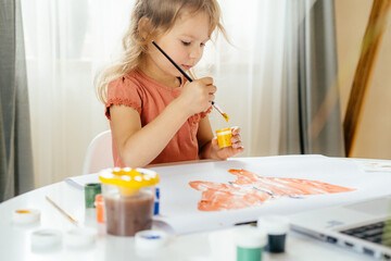 The girl spending a time drawing the picture using laptop at home. Distance learning, online education.